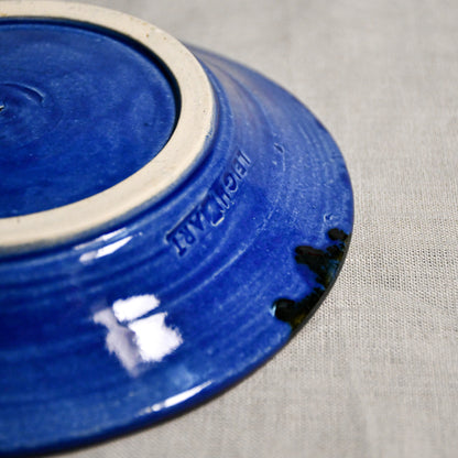 Close up of bottom of a blue ceramic saucer showing exposed stoneware clay foot and texture