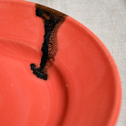 Close up of coral handmade wheelthrown pottery saucer with black drips from the 5th Buffalo collection by Leigh Art