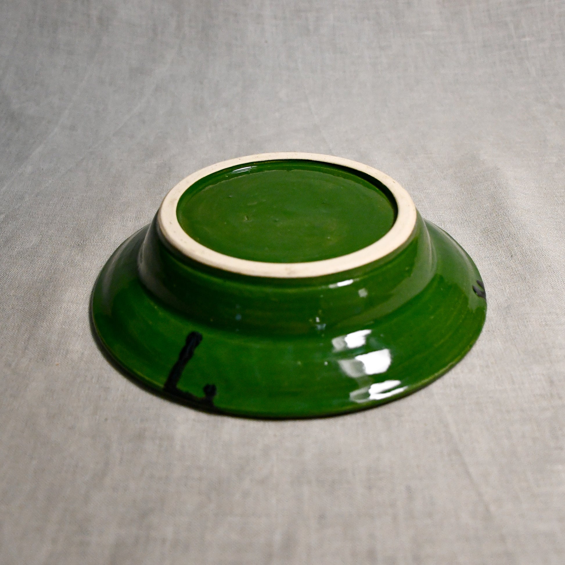 Close up of bottom of a green ceramic saucer showing exposed stoneware clay foot and texture