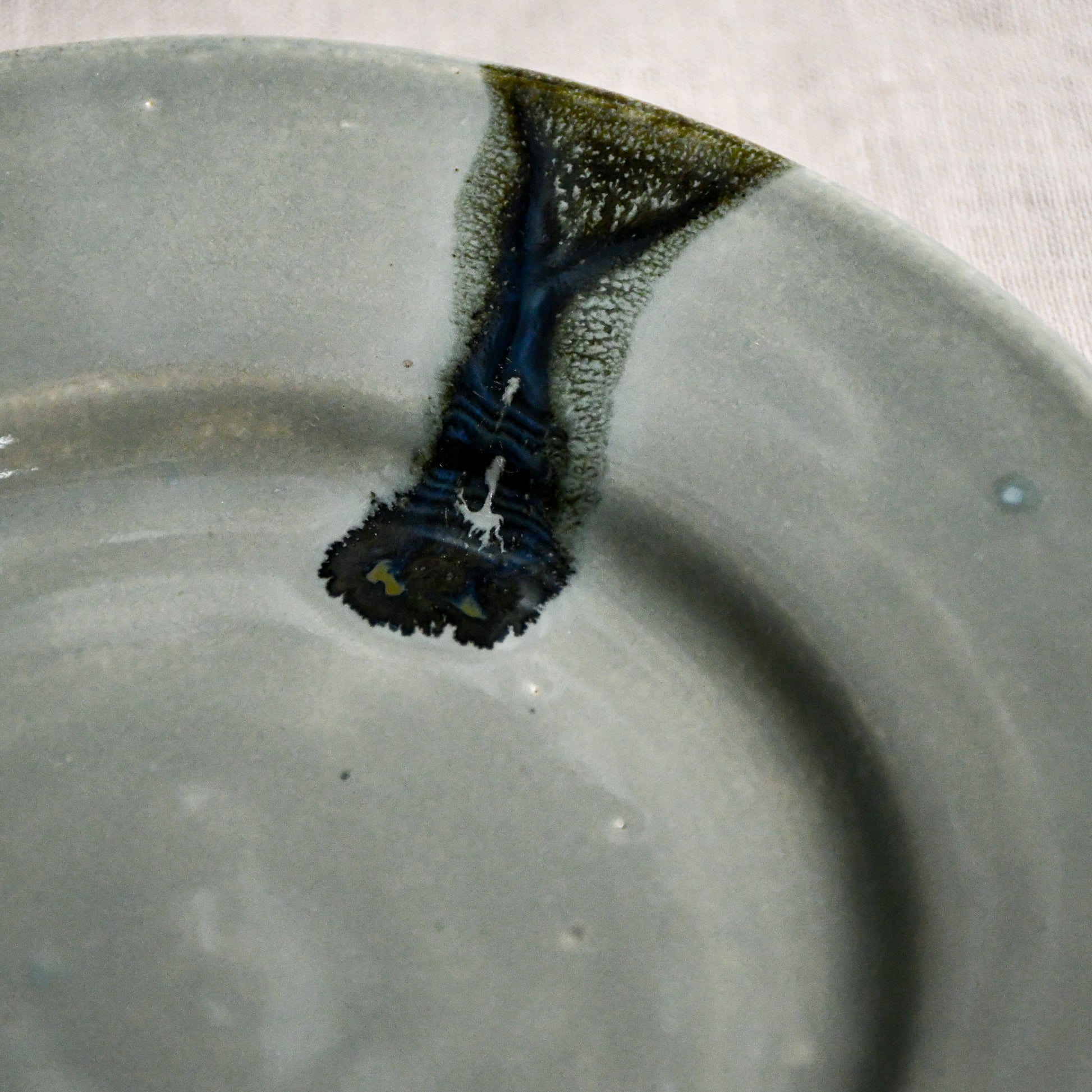 Close up of grey handmade wheelthrown pottery saucer with black drips from the 5th Buffalo collection by Leigh Art