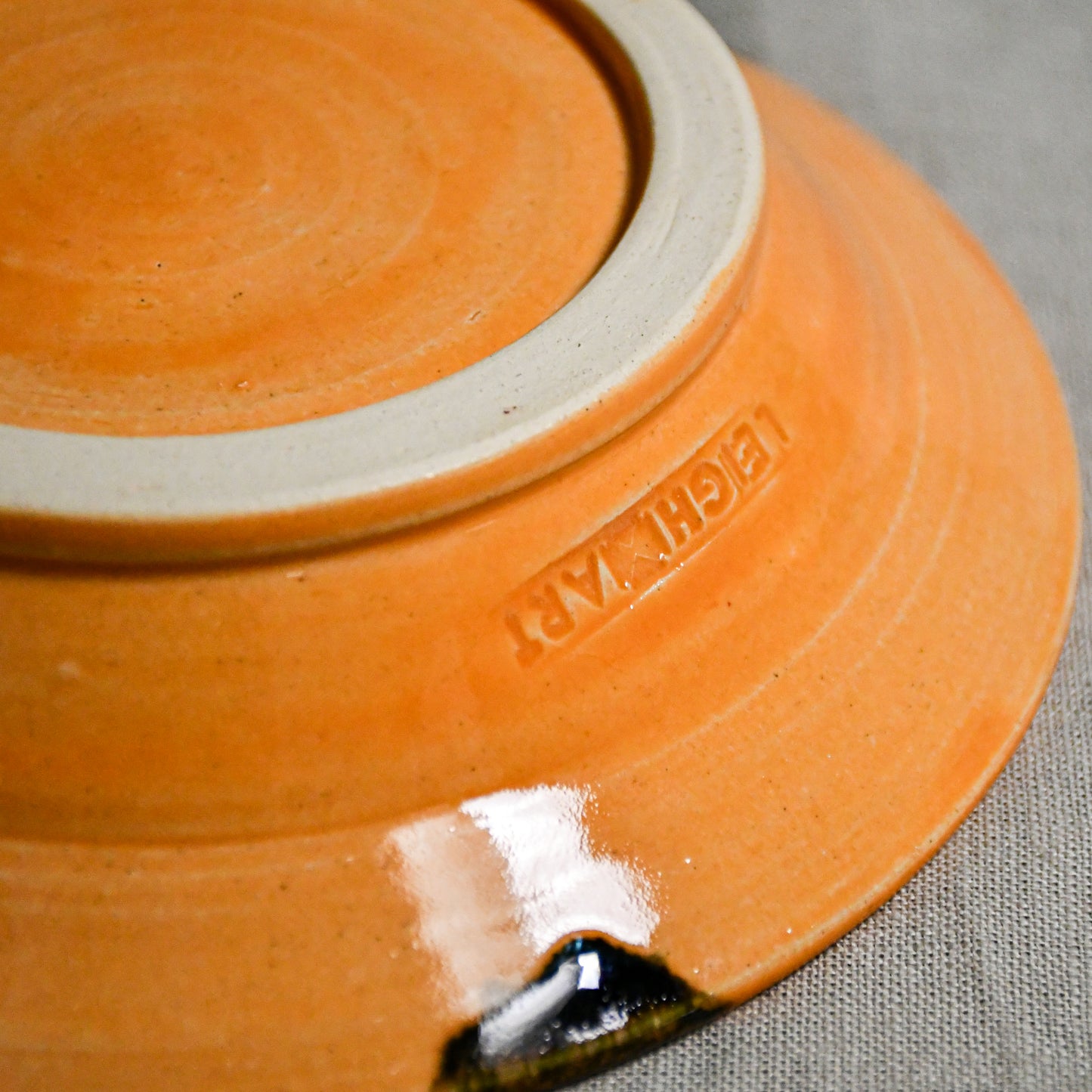 Close up of bottom of a orange ceramic saucer showing exposed stoneware clay foot and texture