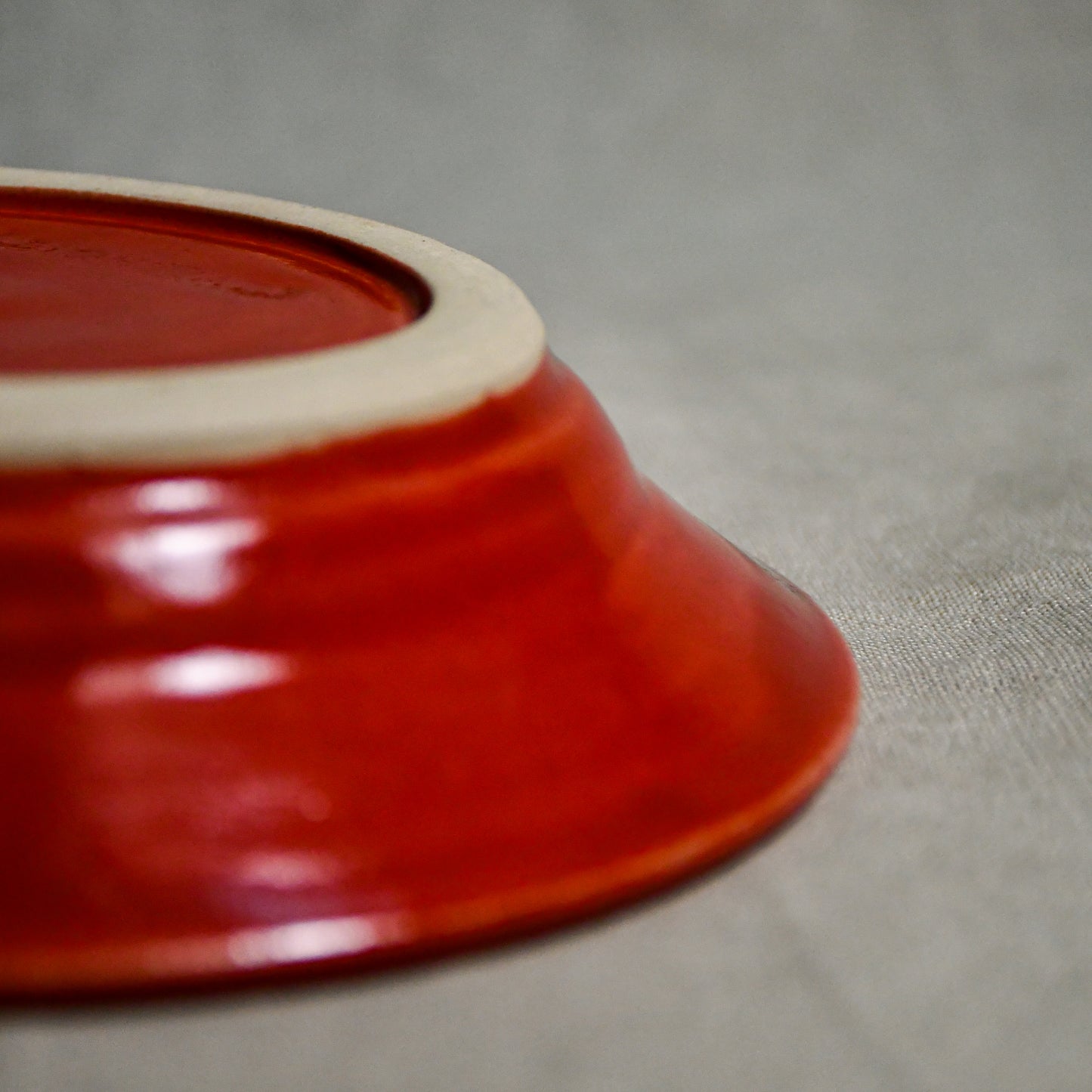Close up of bottom of a red ceramic saucer showing exposed stoneware clay foot and texture