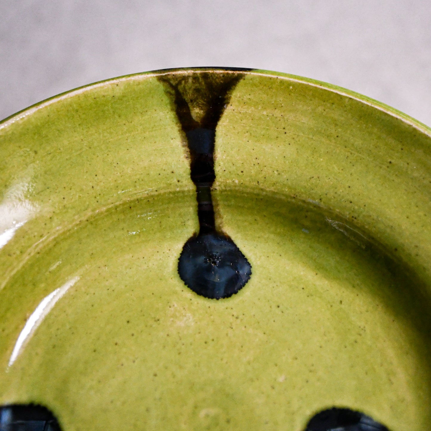 Close up of lime green handmade wheelthrown pottery saucer with black drips from the 5th Buffalo collection by Leigh Art