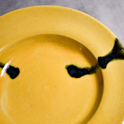 Close up of yellow handmade wheelthrown pottery saucer with black drips and crazing from the 5th Buffalo collection by Leigh Art