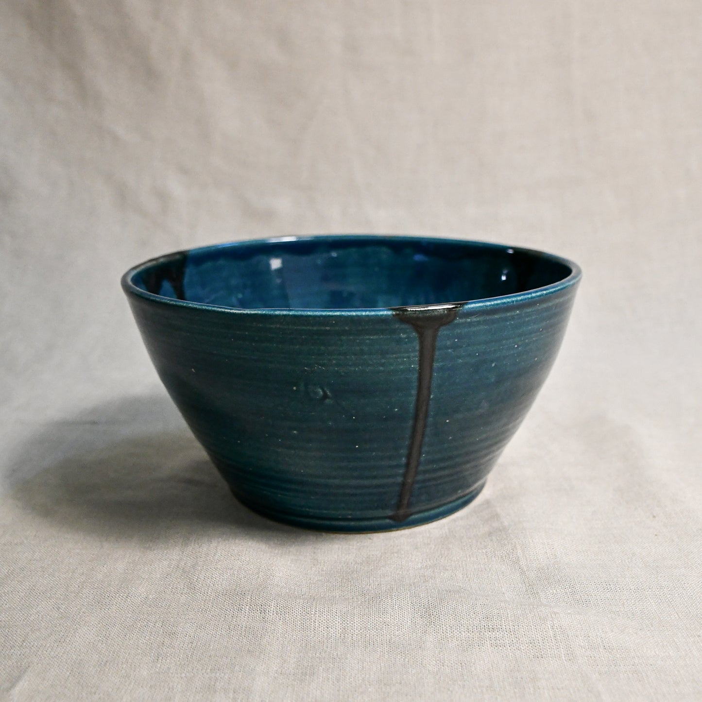 Side view of dark teal handmade wheelthrown serving bowl with black drips from the 5th Buffalo collection from Leigh Art. 