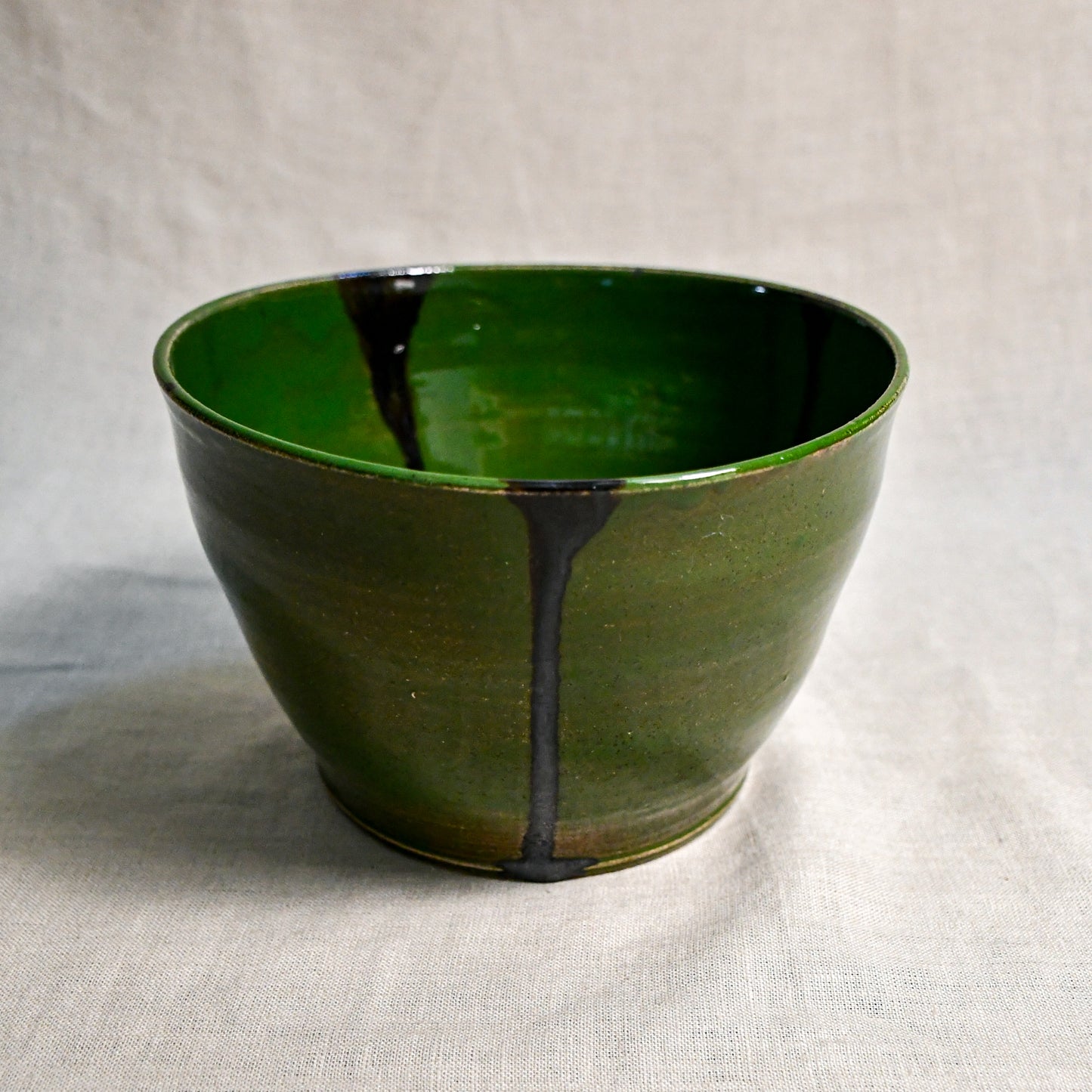 Side view of green handmade wheelthrown serving bowl with black drips from the 5th Buffalo collection from Leigh Art. 