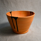 Side view of orange handmade wheelthrown serving bowl with black drips from the 5th Buffalo collection from Leigh Art. 