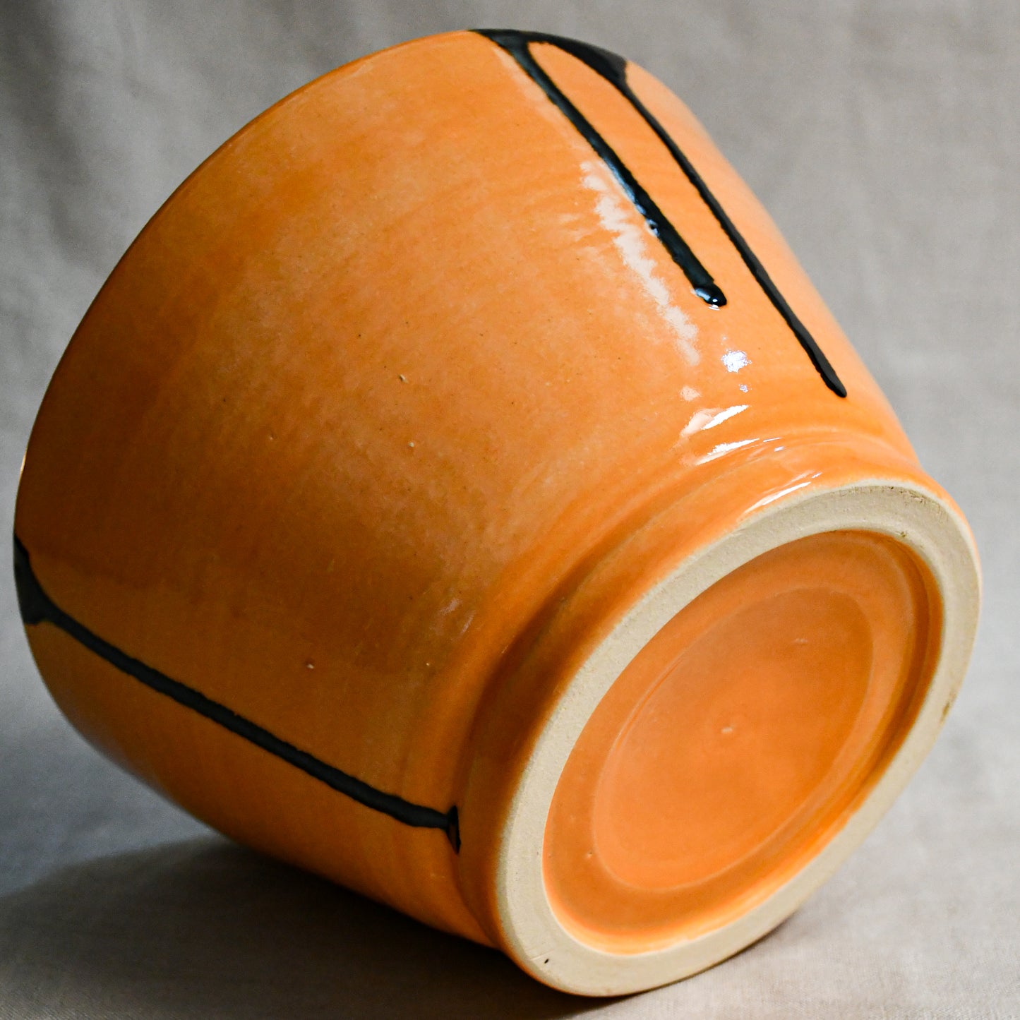Bottom view of orange handmade wheelthrown serving bowl with black drips from the 5th Buffalo collection from Leigh Art. 