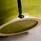 Close up bottom view of lime green handmade wheelthrown serving bowl with black drips and texture from the 5th Buffalo collection from Leigh Art. 