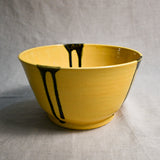 Side view of yellow handmade wheelthrown serving bowl with black drips from the 5th Buffalo collection from Leigh Art. 