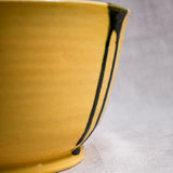Close up of yellow handmade wheelthrown serving bowl with black drips and texture from the 5th Buffalo collection from Leigh Art. 