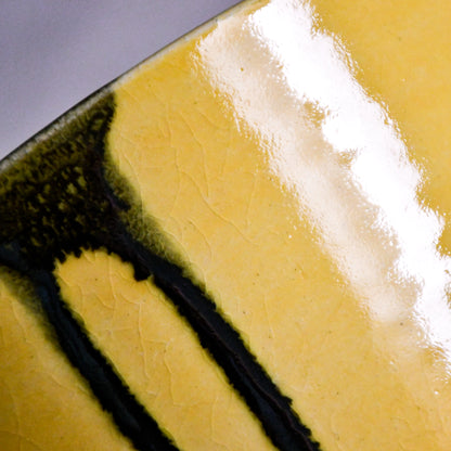 Close up of yellow handmade wheelthrown serving bowl with black drips and crazing from the 5th Buffalo collection from Leigh Art. 