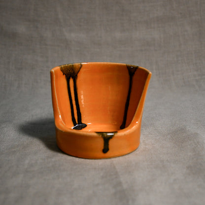 Close up of orange vertical handmade pottery spoon rest from the 5th Buffalo collection by Leigh Art with black drips 