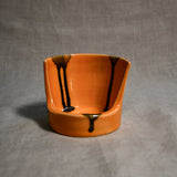 Close up of orange vertical handmade pottery spoon rest from the 5th Buffalo collection by Leigh Art with black drips 