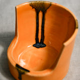 Close up of orange vertical handmade pottery spoon rest from the 5th Buffalo collection by Leigh Art with black drips and texture