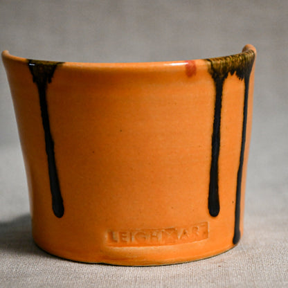 Close up of orange vertical handmade pottery spoon rest from the 5th Buffalo collection by Leigh Art with black drips and texture