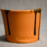 Close up of orange vertical handmade pottery spoon rest from the 5th Buffalo collection by Leigh Art with black drips and texture