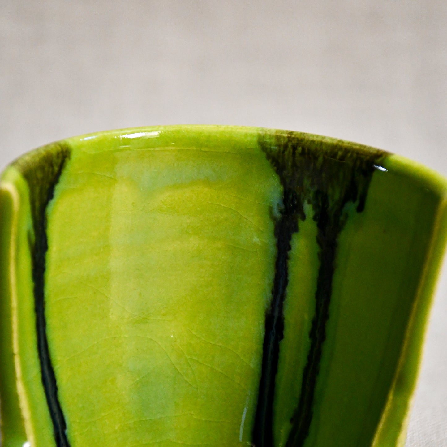 Close up of lime green vertical handmade pottery spoon rest from the 5th Buffalo collection by Leigh Art with black drips and crazing