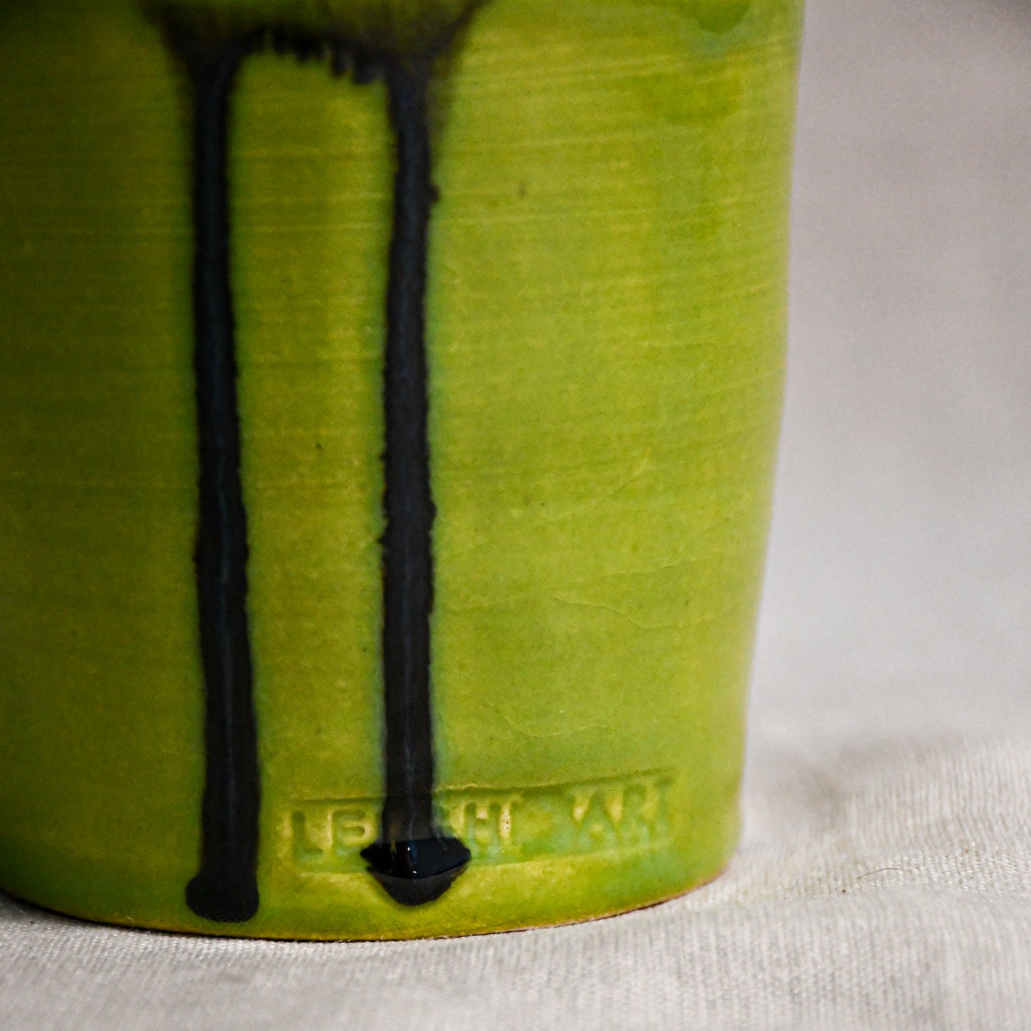 Close up of lime green vertical handmade pottery spoon rest from the 5th Buffalo collection by Leigh Art with black drips, crazing, and texture.