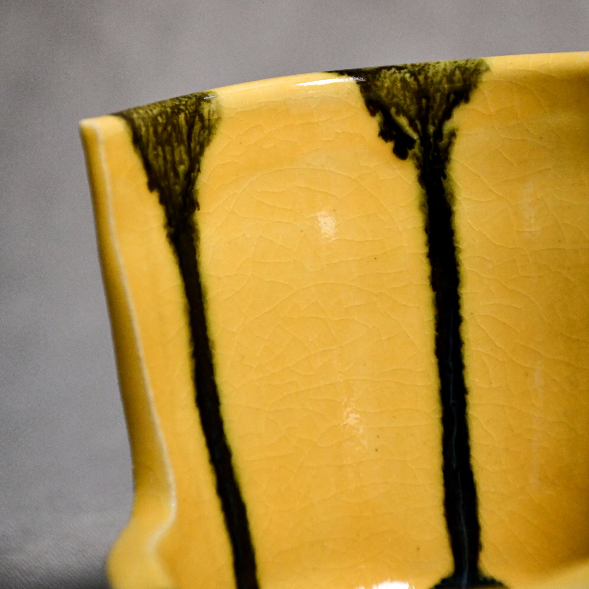 Close up of yellow vertical handmade pottery spoon rest from the 5th Buffalo collection by Leigh Art with black drips and crazing