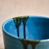 Close-up of black glaze drips and crazing on a turquoise handmade pottery bowl