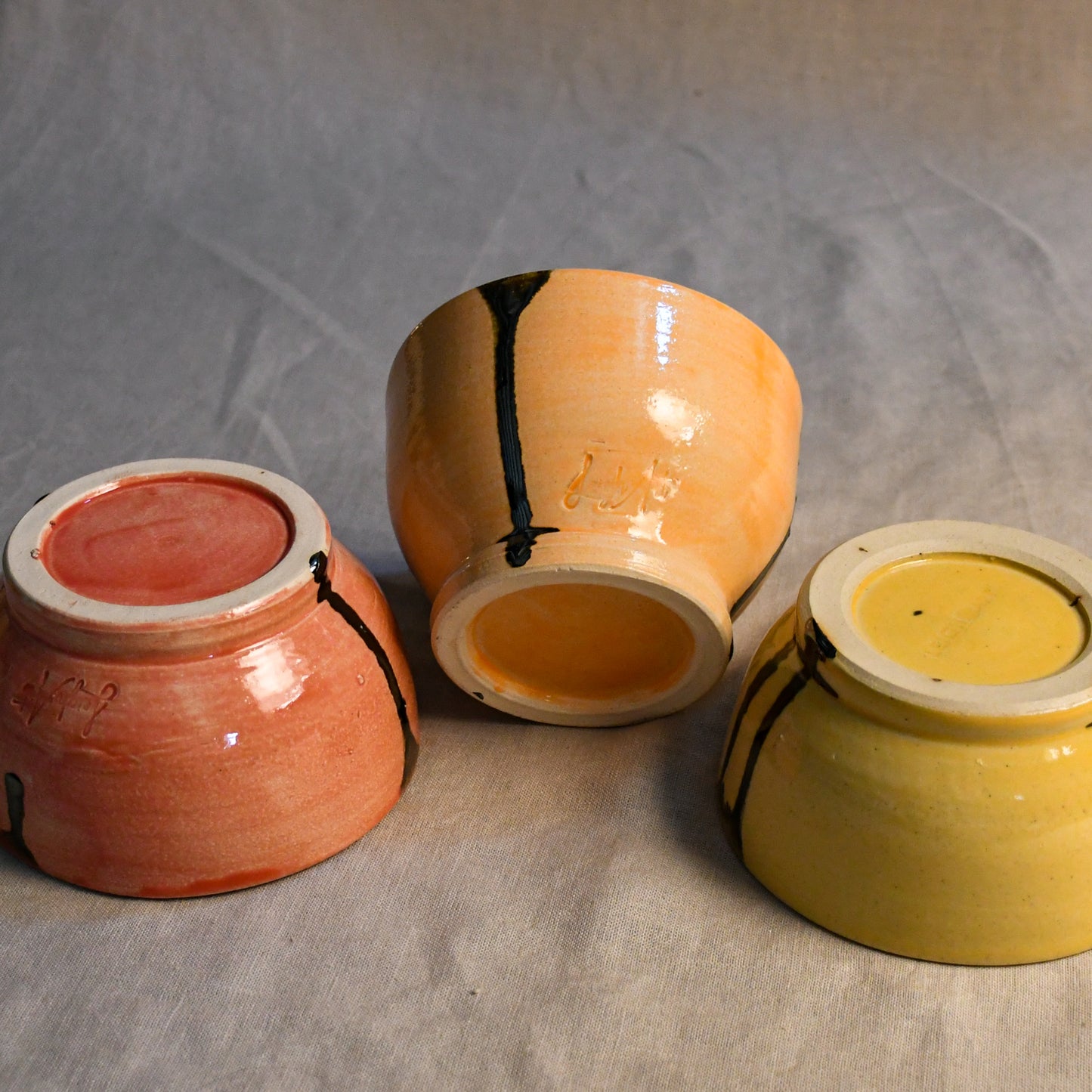 5th Buffalo soft finish chili bowls showing their feet in Coral, Jack O'Lantern, and Dandelion colors with black drips.
