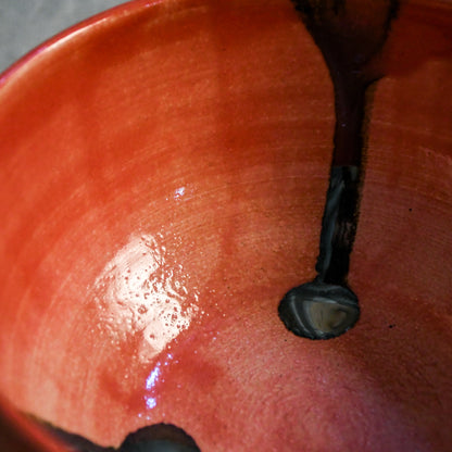 Close-up of a glossy terracotta orange ceramic bowl interior with a dark brown painted vertical accent and a small circular opening.