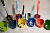 Collection of vertical spoon rests in 9 colors with various kitchen utensils standing in them from Leigh Art. 