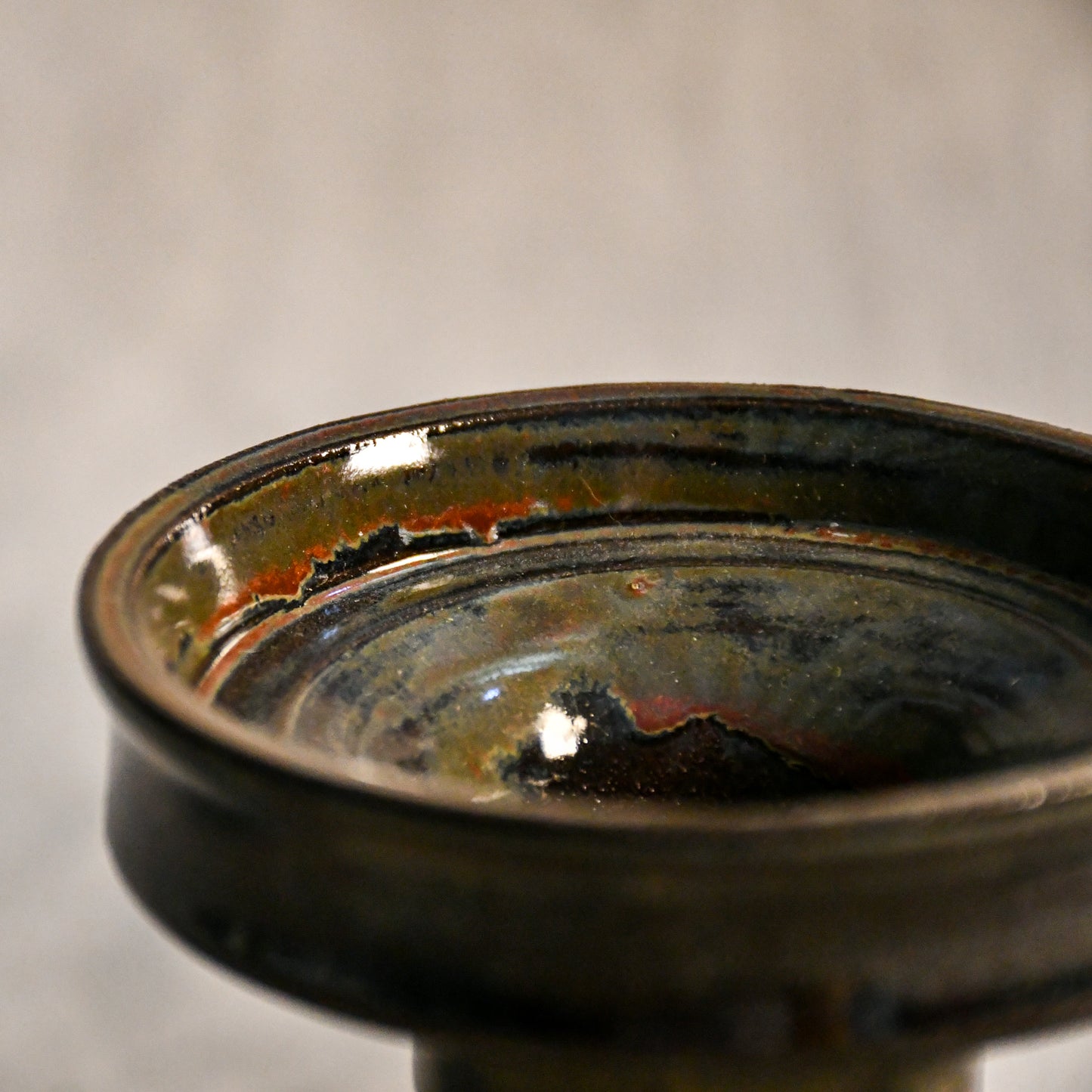 Close-up of the Ancient Jasper glaze on a handmade ceramic candlestick, showcasing layered tones of black, bronze, olive green, and rust with a glossy finish.