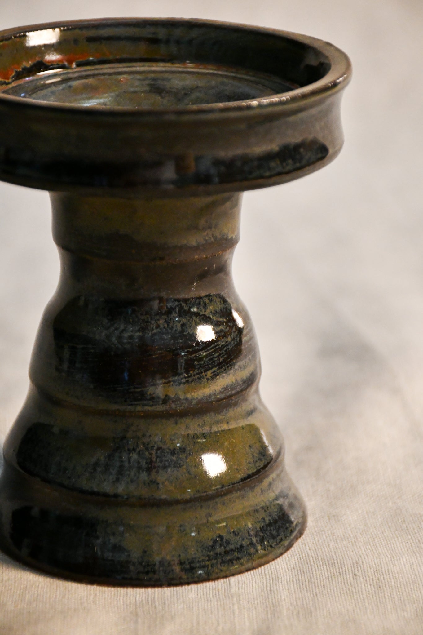 Close-up of the Ancient Jasper glaze on a handmade ceramic candlestick, showcasing layered tones of black, bronze, olive green, and rust with a glossy finish.