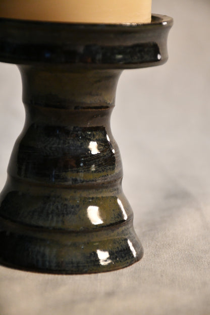 Close-up of the Ancient Jasper glaze on a handmade ceramic candlestick, showcasing layered tones of black, bronze, olive green, and rust with a glossy finish.