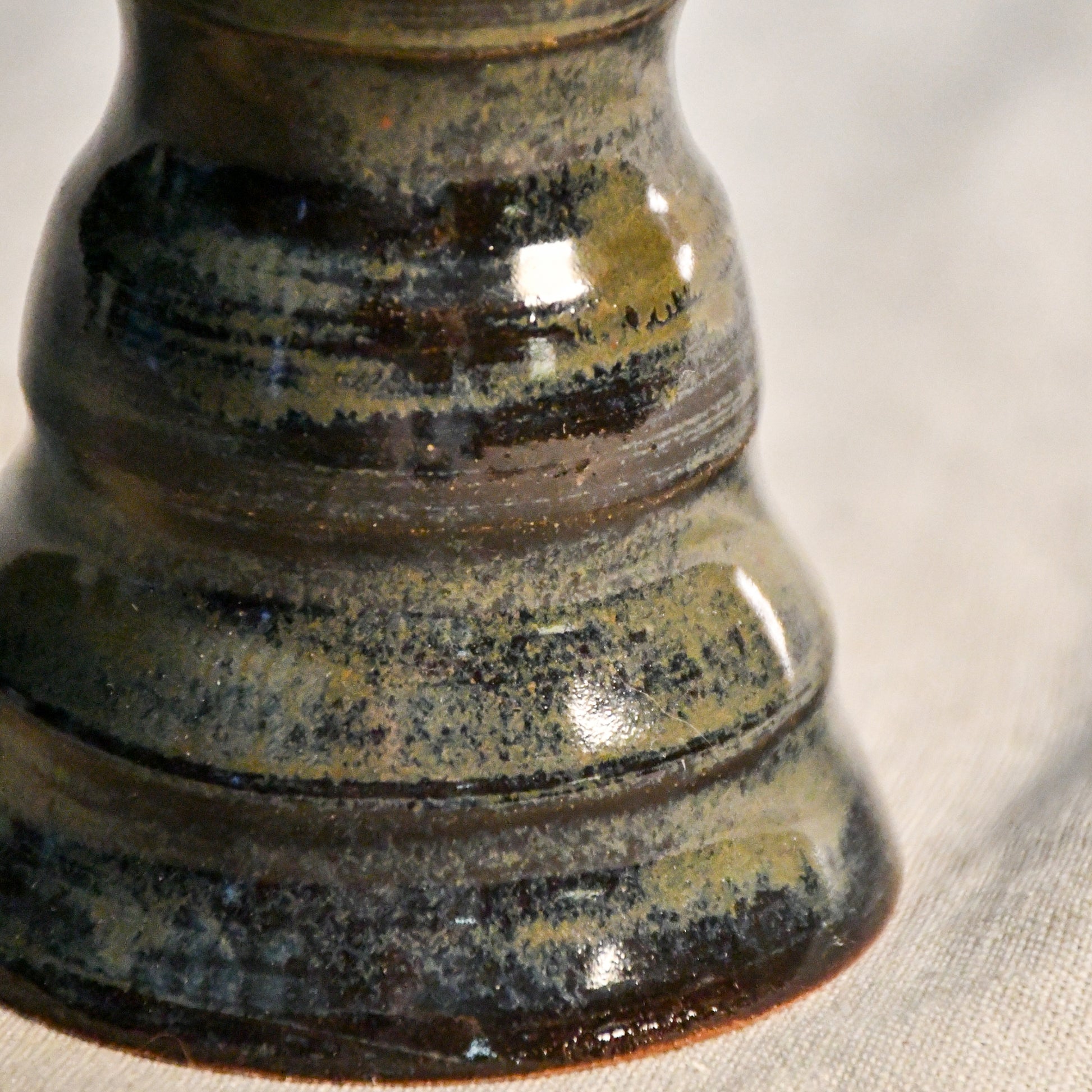 Close-up of the Ancient Jasper glaze on a handmade ceramic candlestick, showcasing layered tones of black, bronze, olive green, and rust with a glossy finish.