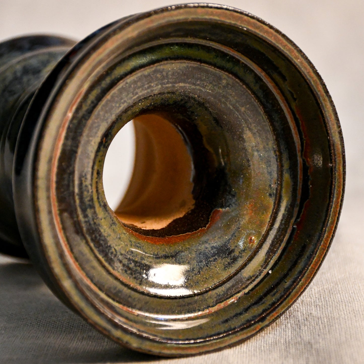 Top view: Close-up of the Ancient Jasper glaze on a handmade ceramic candlestick, showcasing layered tones of black, bronze, olive green, and rust with a glossy finish.