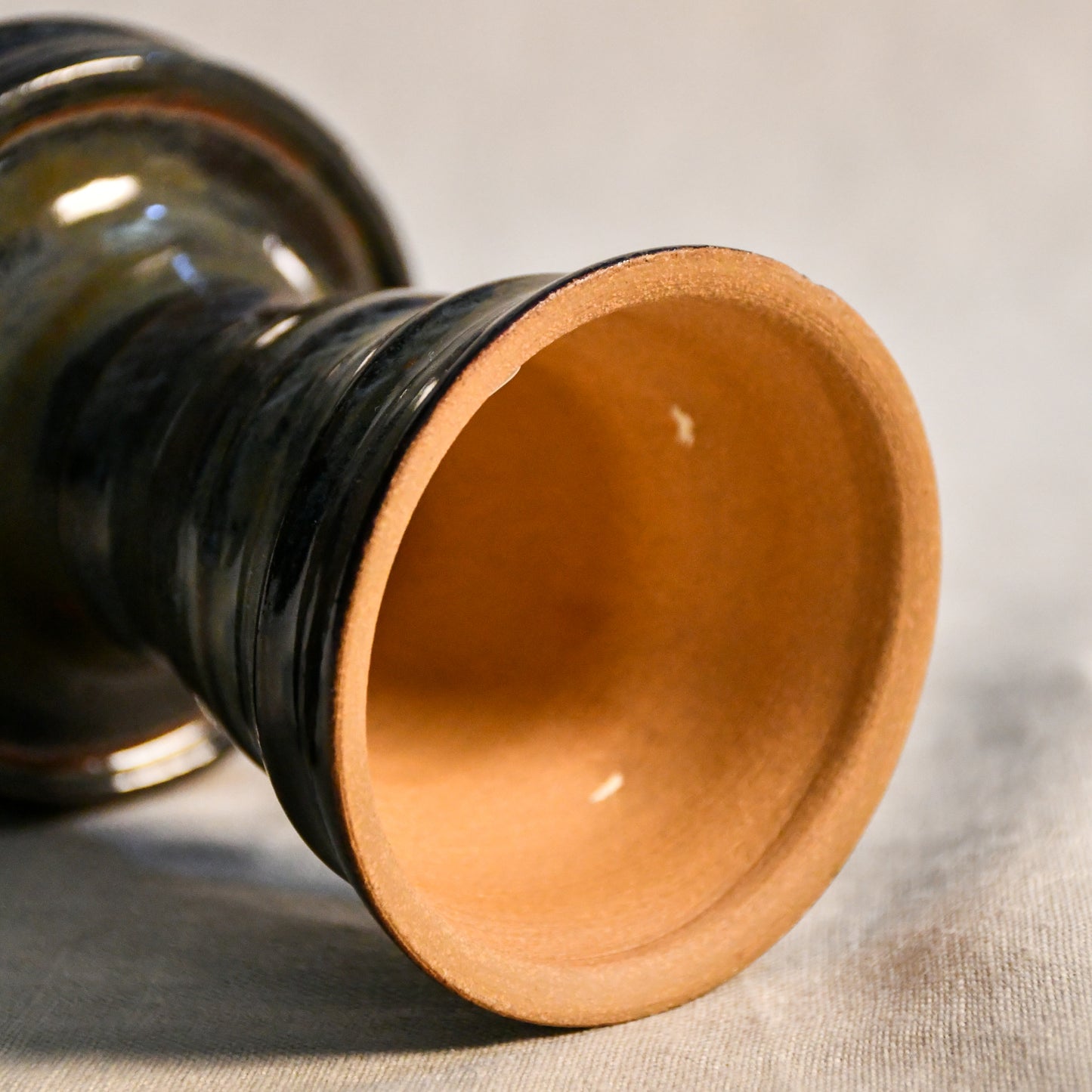 Bottom View: Close-up of the Ancient Jasper glaze on a handmade ceramic candlestick, showcasing layered tones of black, bronze, olive green, and rust with a glossy finish.