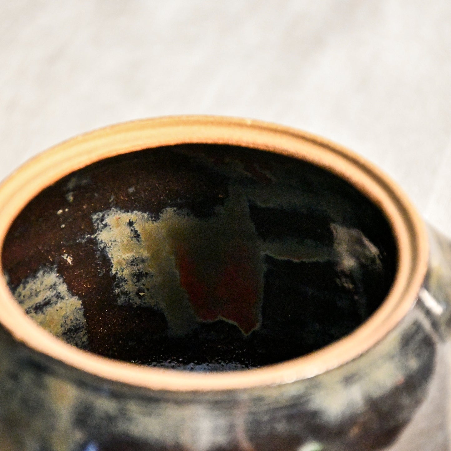 Close-up of the Ancient Jasper glaze on a handmade ceramic teapot, showcasing glossy layers of bronze, olive green, black, and deep rust tones.