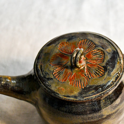 Close-up of the stamped lid on the Ancient Jasper ceramic teapot, highlighting layered rust, olive, and black glaze variations.