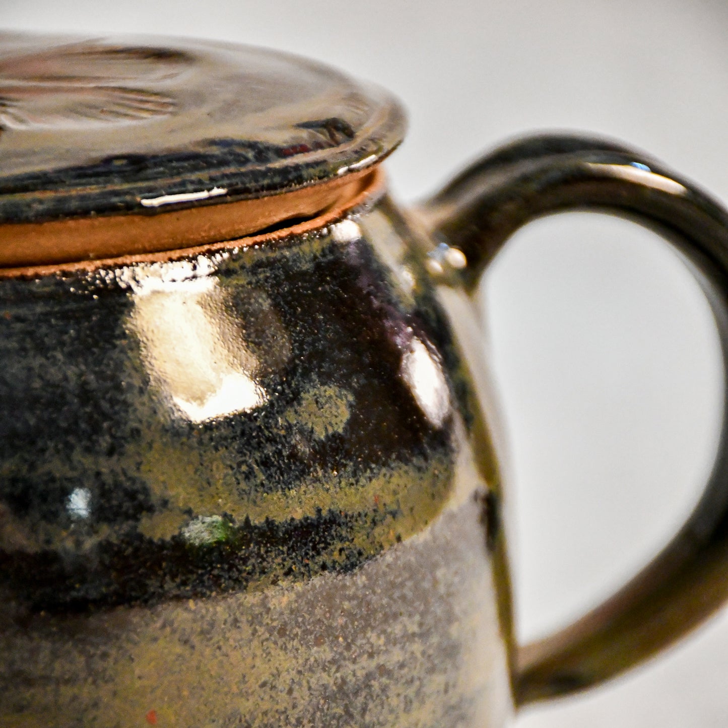 Close-up of the Ancient Jasper glaze on a handmade ceramic teapot, showcasing glossy layers of bronze, olive green, black, and deep rust tones.