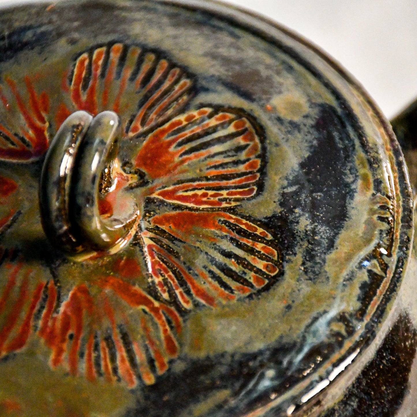 Close-up of the stamped lid on the Ancient Jasper ceramic teapot, highlighting layered rust, olive, and black glaze variations.