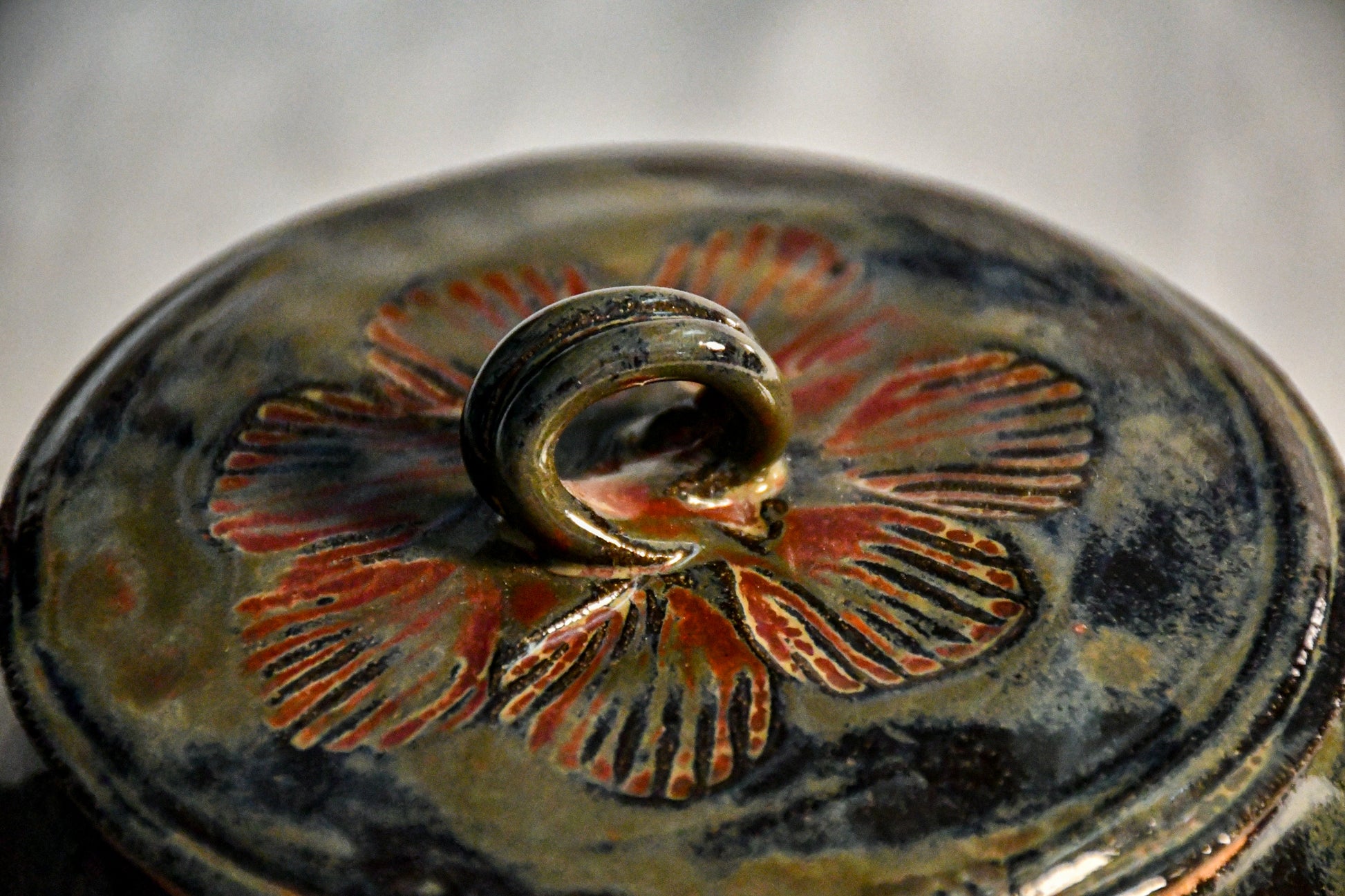 Detailed view of the stamped motif on the Ancient Jasper teapot lid with a sculpted loop handle and flowing glaze movement.