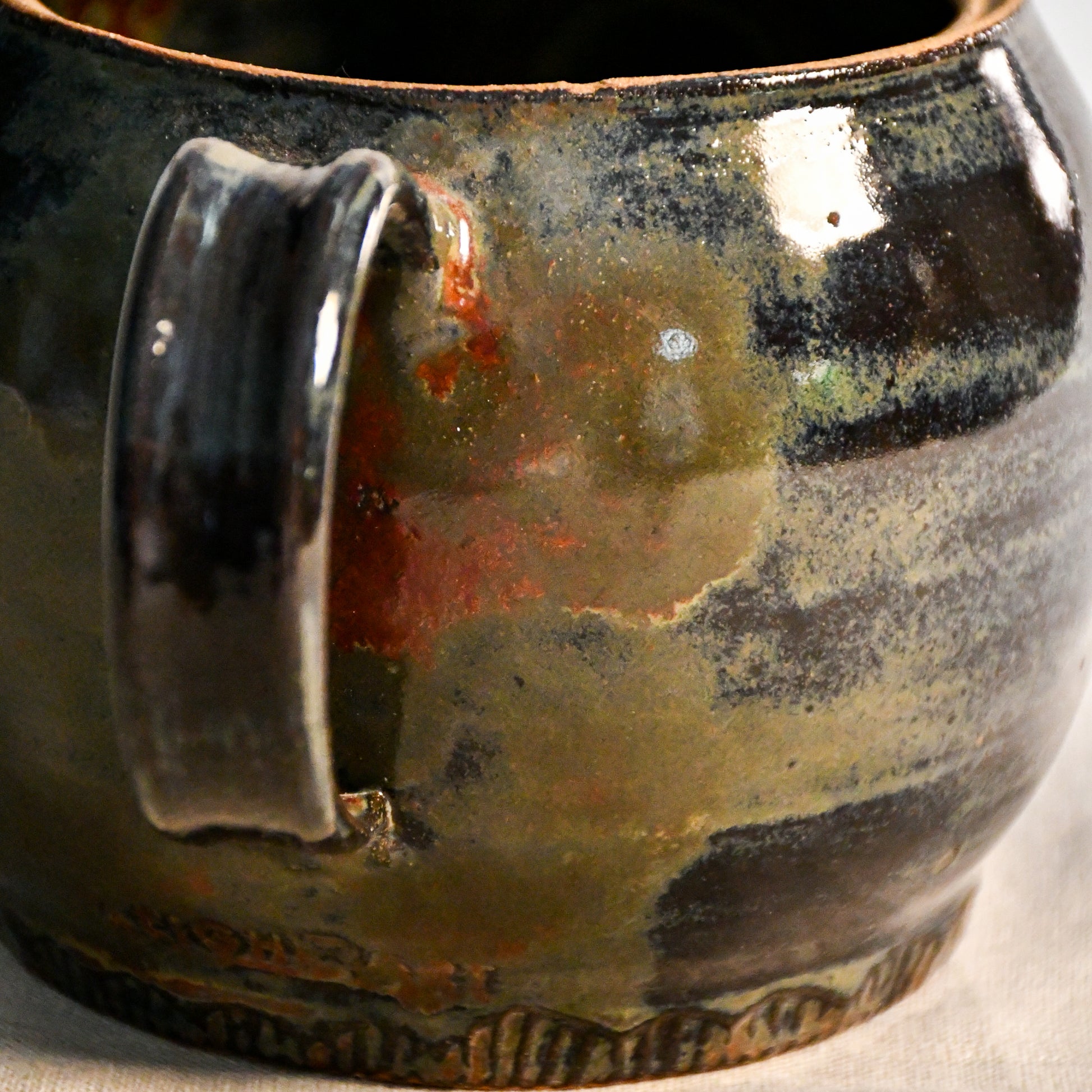 Close-up of the Ancient Jasper glaze on a handmade ceramic teapot, showcasing glossy layers of bronze, olive green, black, and deep rust tones.