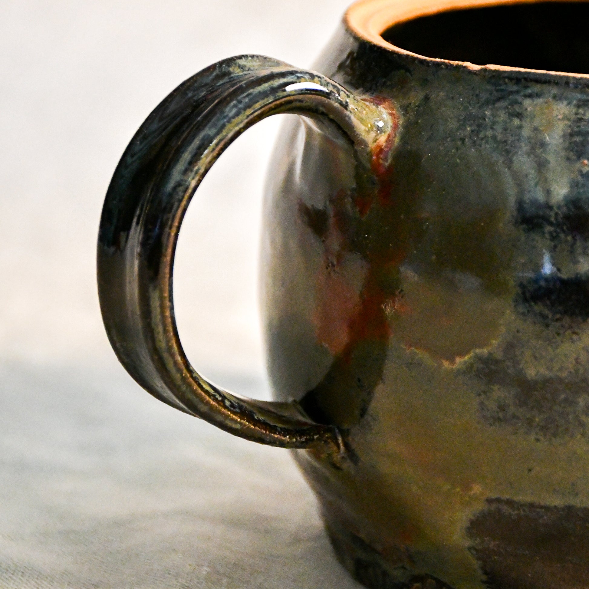 Close-up of the Ancient Jasper glaze on a handmade ceramic teapot, showcasing glossy layers of bronze, olive green, black, and deep rust tones.