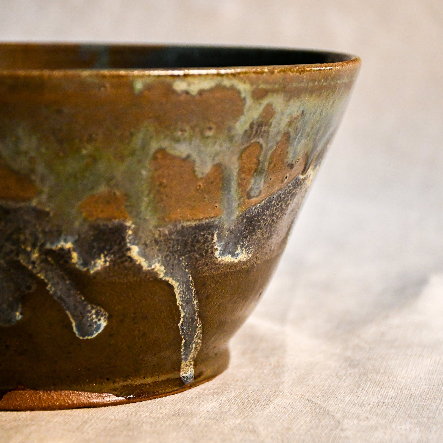 Close-up of the Espuela glaze on a handmade serving bowl, showcasing flowing earth tones and unique kiln effects.