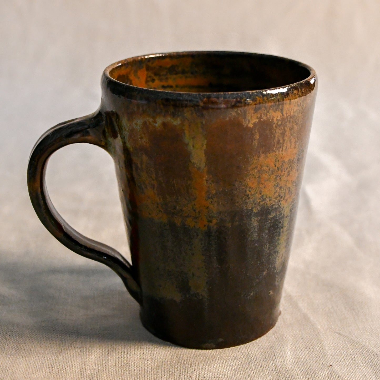 Handmade wheel-thrown stoneware mug glazed in Ancient Jasper, featuring layered tones of rust orange, smoky black, olive green, and rich brown.