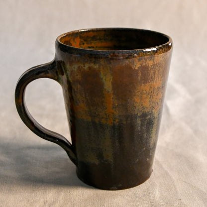 Handmade wheel-thrown stoneware mug glazed in Ancient Jasper, featuring layered tones of rust orange, smoky black, olive green, and rich brown.