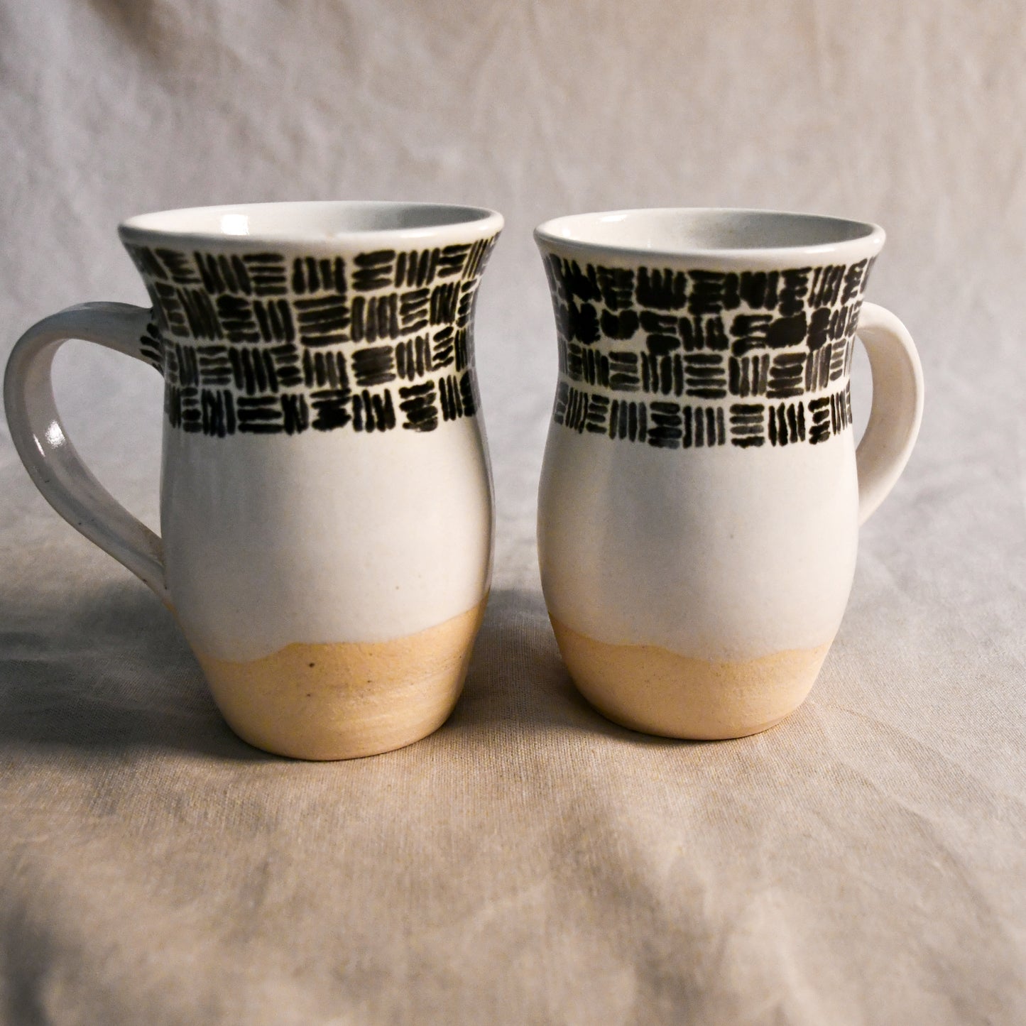 Handmade pottery mug with a curved silhouette, comfortable handle, creamy white glaze, and black abstract brushstroke decoration.