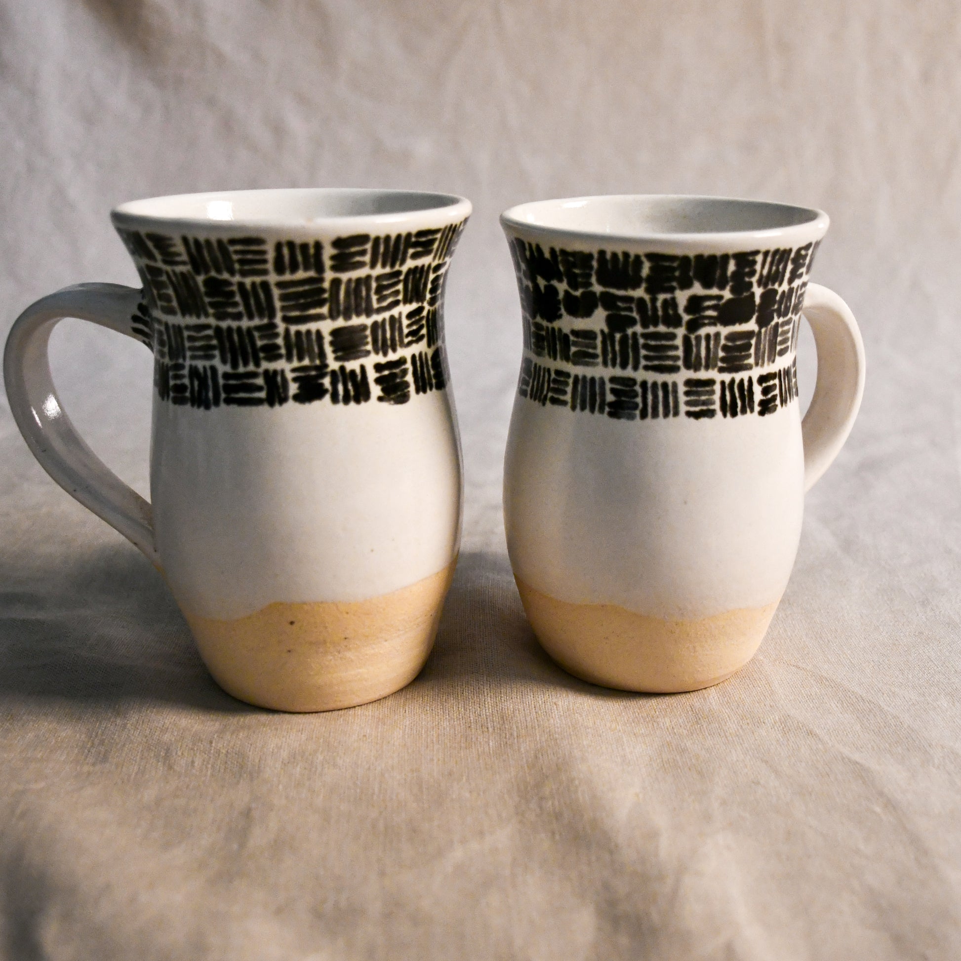 Handmade pottery mug with a curved silhouette, comfortable handle, creamy white glaze, and black abstract brushstroke decoration.