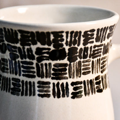 Close-up of the hand-painted black brushstroke pattern wrapping around a handmade stoneware mug beneath the rim.
