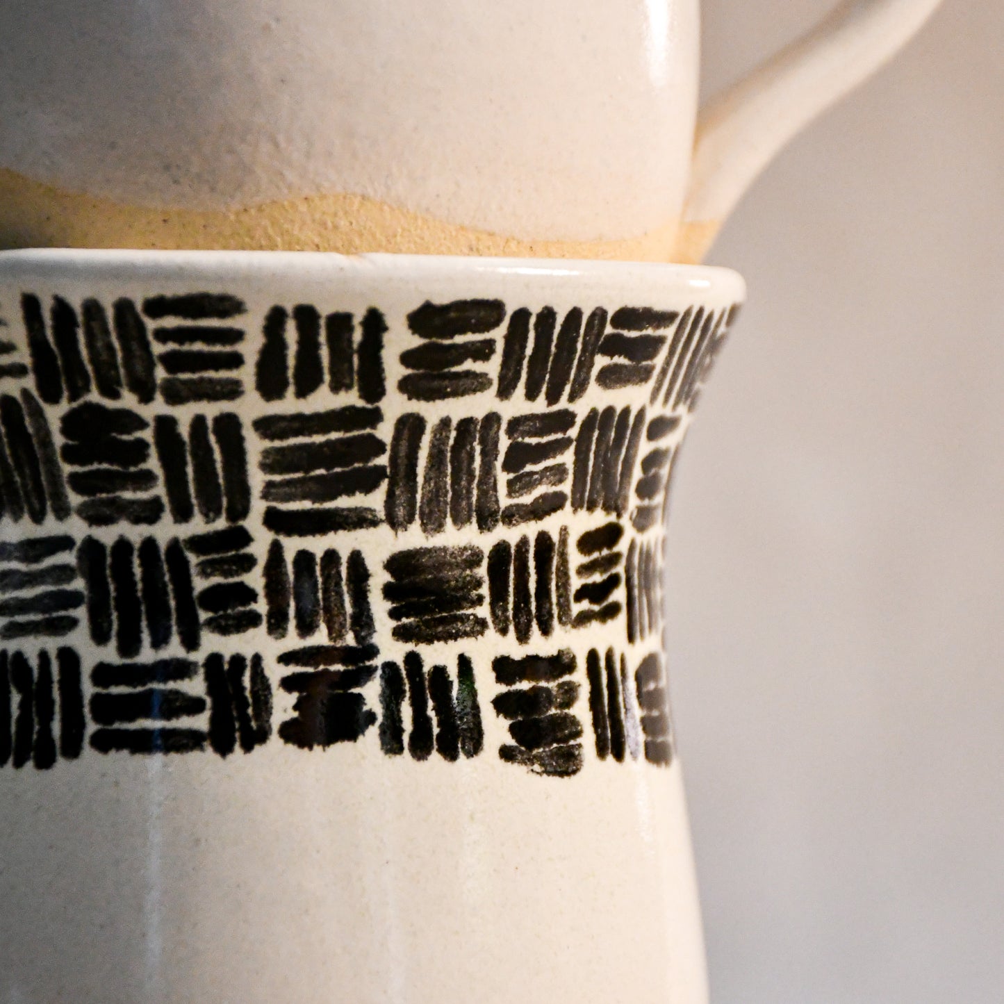 Close-up of the hand-painted black brushstroke pattern wrapping around a handmade stoneware mug beneath the rim.