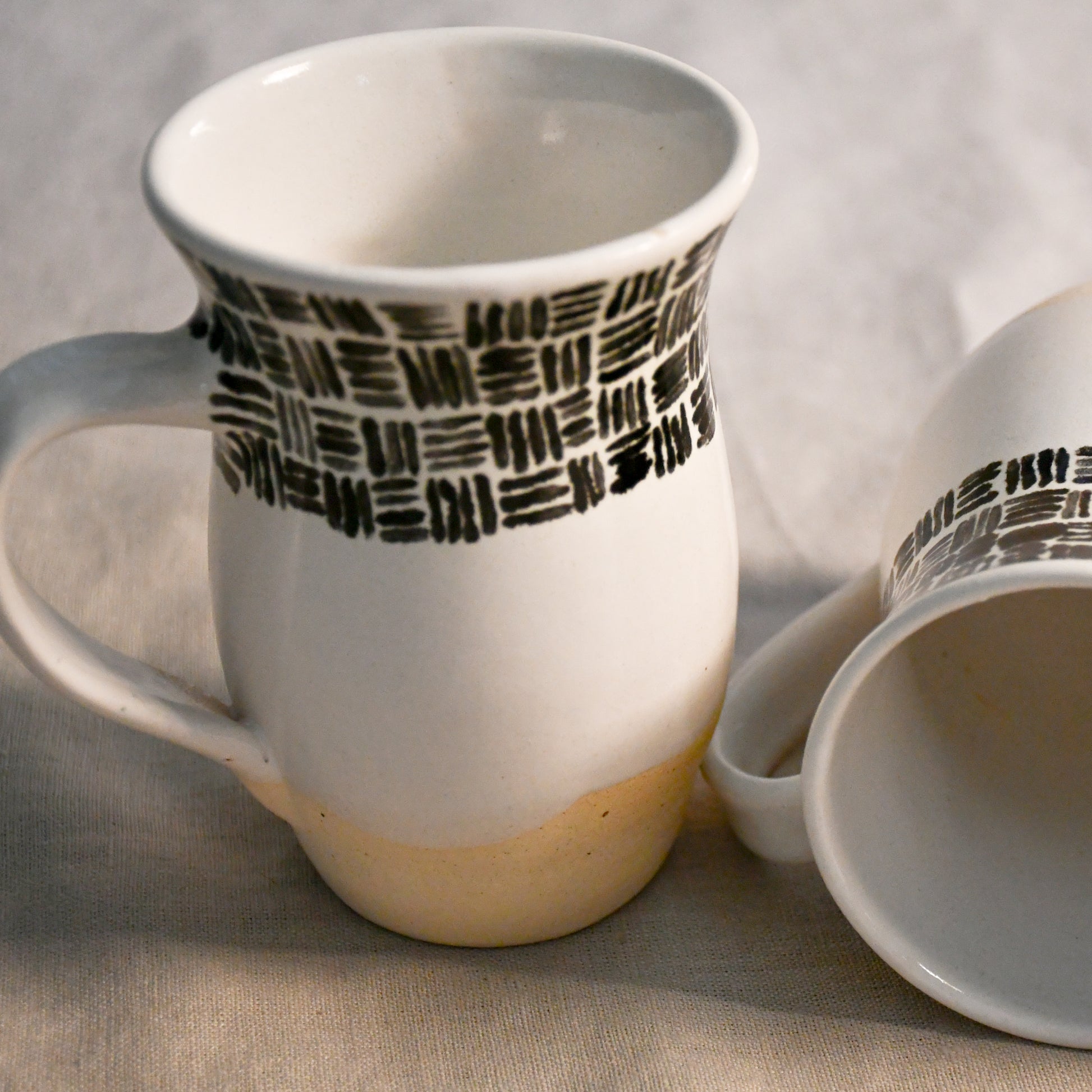 Handmade ceramic mugs with glossy white interiors and softly flared rims designed for everyday use.