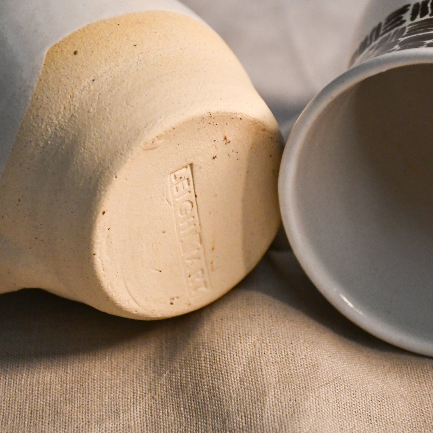 Underside of a handmade pottery mug featuring the Leigh Art maker's mark impressed into the unglazed clay foot.